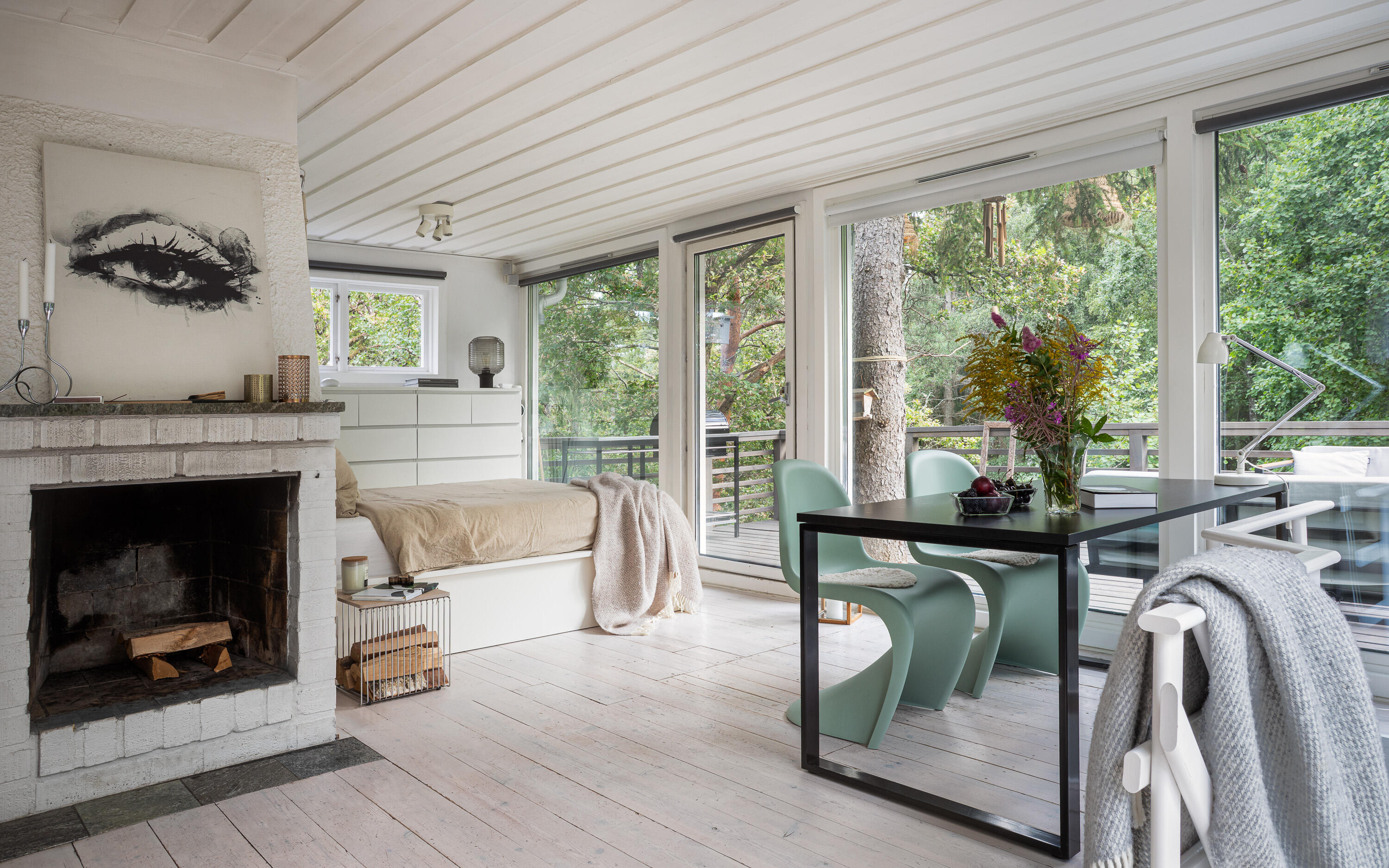Bright woodland cabin interior with a white fireplace, dining table and floor-to-ceiling windows. Bright woodland cabin interior with a white fireplace, dining table and floor-to-ceiling windows.