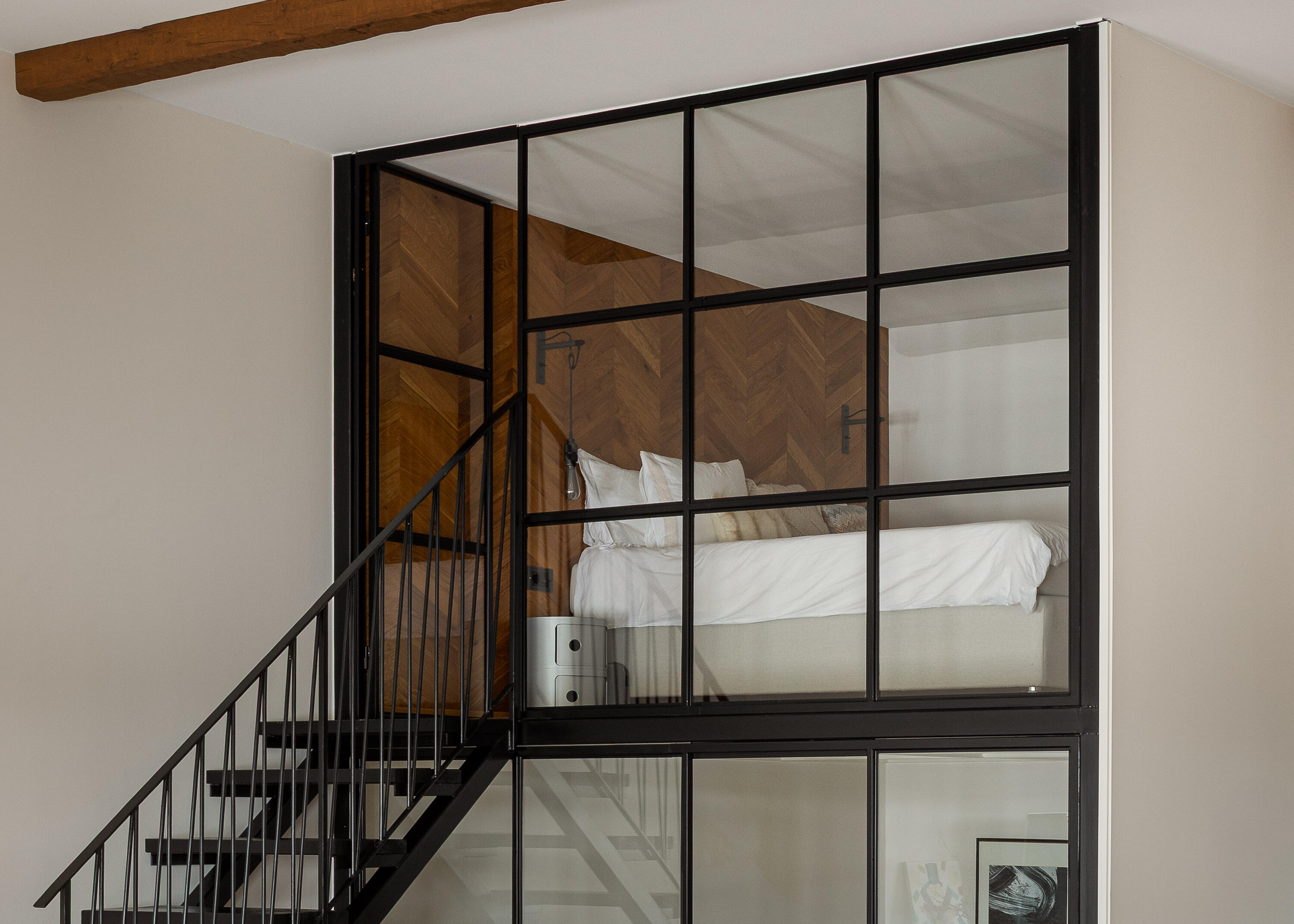 Mezzanine bedroom behind a black steel-framed glass wall. Mezzanine bedroom behind a black steel-framed glass wall.