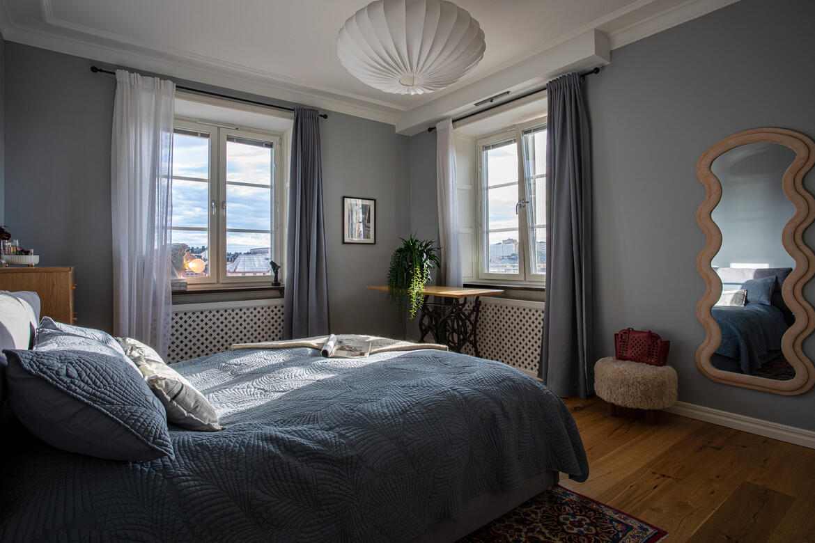 Blue bedroom with blue bedding, corner windows and a sculptural mirror. Blue bedroom with blue bedding, corner windows and a sculptural mirror.