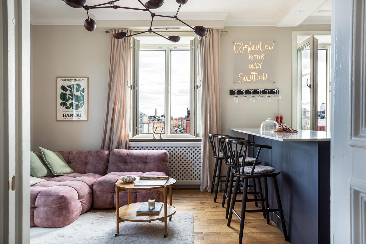 View through a doorway to a pink sofa and blue kitchen in a bright city apartment. View through a doorway to a pink sofa and blue kitchen in a bright city apartment.