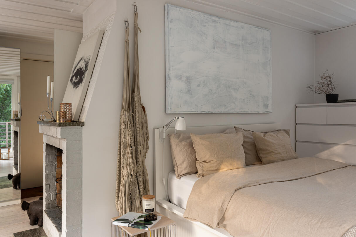 Neutral bedroom nook beside a white brick fireplace in a Scandinavian woodland cabin. Neutral bedroom nook beside a white brick fireplace in a Scandinavian woodland cabin.