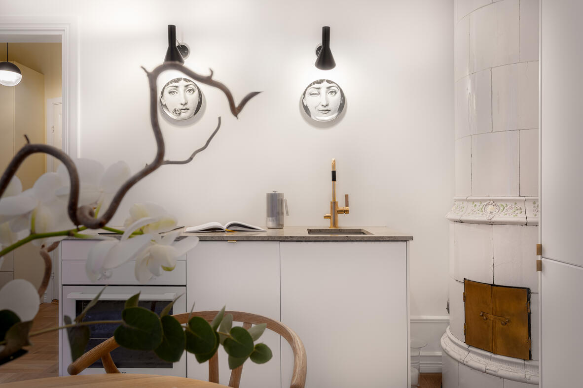 Minimal white kitchen with a tiled stove, brass tap and sculptural Fornasetti wall plates. Minimal white kitchen with a tiled stove, brass tap and sculptural Fornasetti wall plates.
