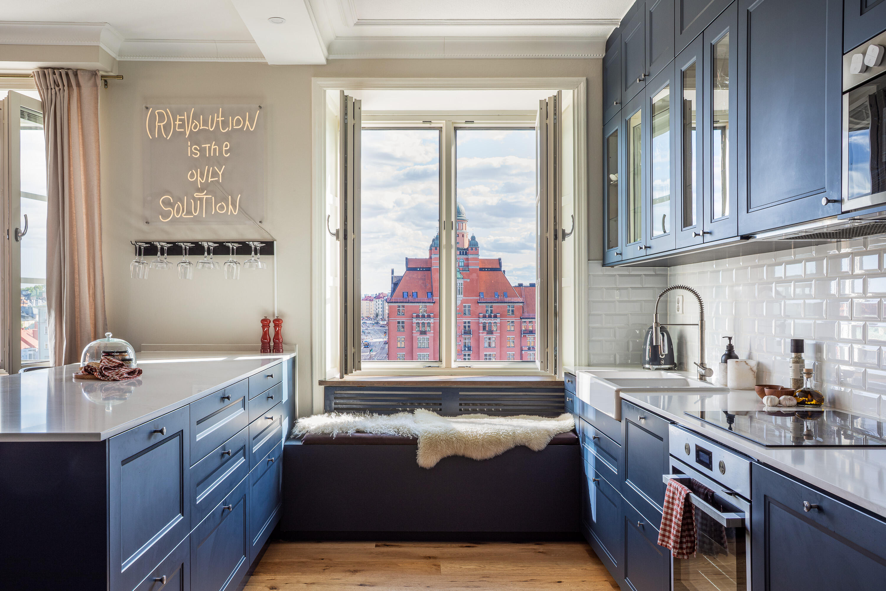 Blue kitchen with a window seat, city view and neon wall sign. Blue kitchen with a window seat, city view and neon wall sign.